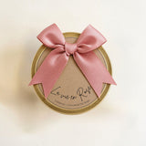 La Vie en Rose Golden Floral Candle made from natural soy wax in a golden candle tin with a soft pink bow and soft floral scent. La Vie en Rose Golden Floral Candle van natuurlijke sojawas in gouden candle tin met roze strik en zachte bloemige geur.